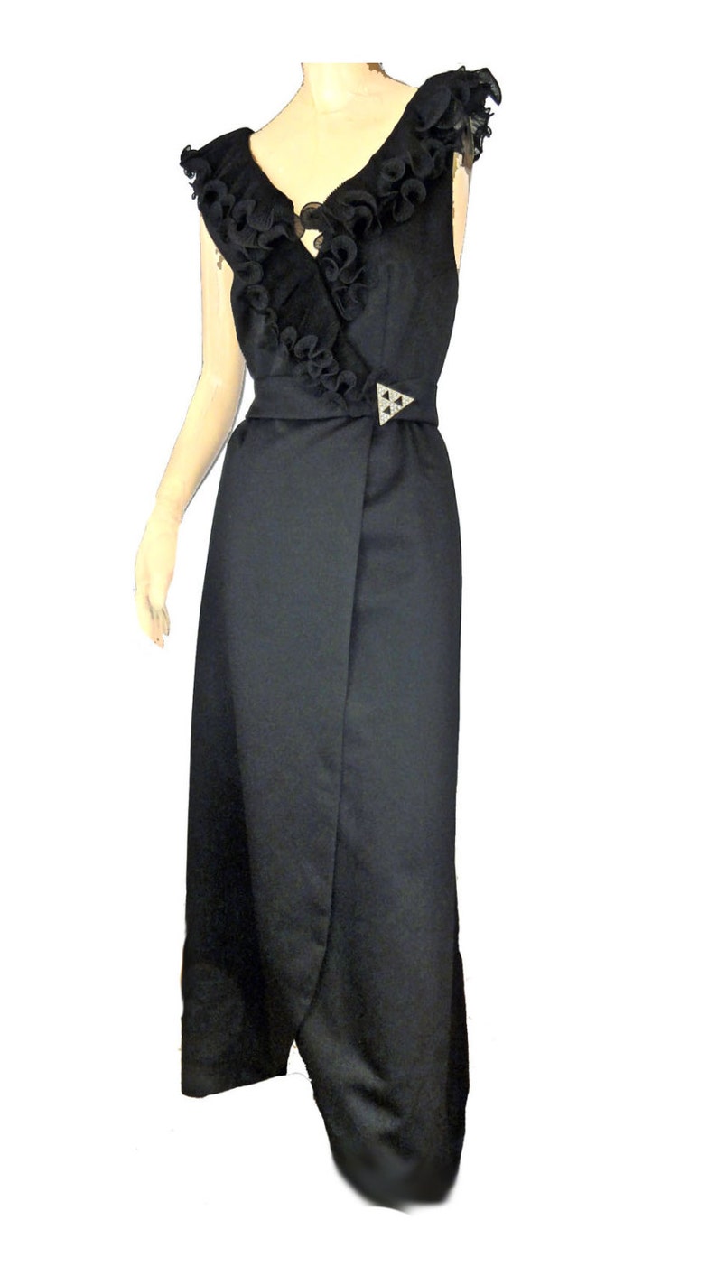 May include: A black sleeveless maxi dress with a ruffled neckline and a wrap-style skirt. The dress has a silver-toned buckle at the waist.