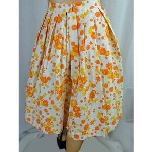 May include: A white skirt with a floral print in orange and yellow. The skirt has a pleated design and a zipper closure in the back.