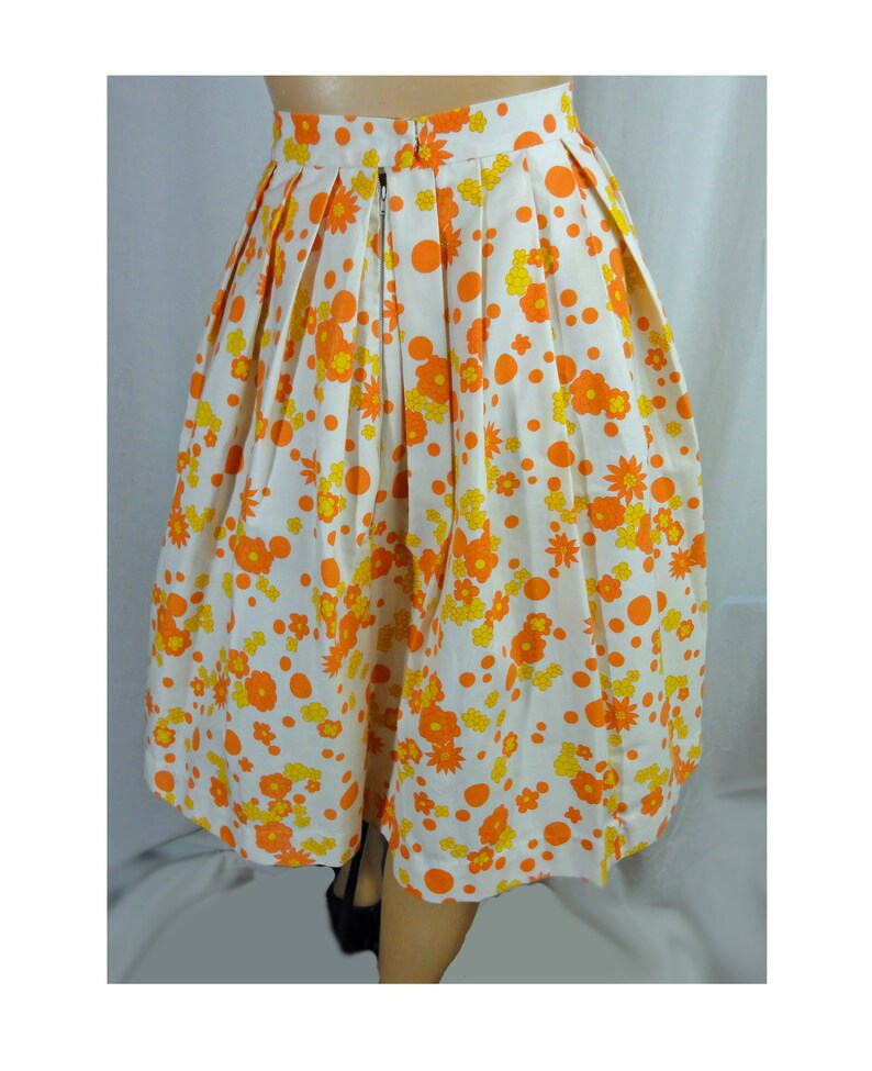 May include: A white skirt with a floral print in orange and yellow. The skirt has a pleated design and a zipper closure in the back.