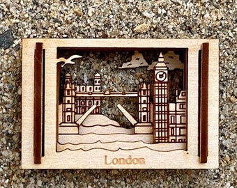 May include: A wooden cutout of the London skyline, featuring Big Ben and Tower Bridge. The cutout is framed in a brown wood frame and has the word "London" printed below the image.