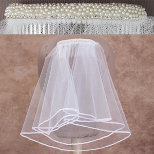 May include: A bridal veil with a comb, featuring a double layer of sheer white fabric. The comb is adorned with faux pearls and rhinestones. The veil is designed to be worn on the head for a wedding or special occasion.