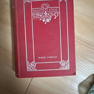 May include: A red hardcover book with a silver title, "The Mighty Atom" by Marie Corelli. The book cover features an ornate silver design.