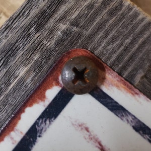 Puede incluir: Primer plano de un tornillo oxidado con cabeza de cruz, que sujeta una pieza de madera a una superficie con un patr&oacute;n blanco y azul.