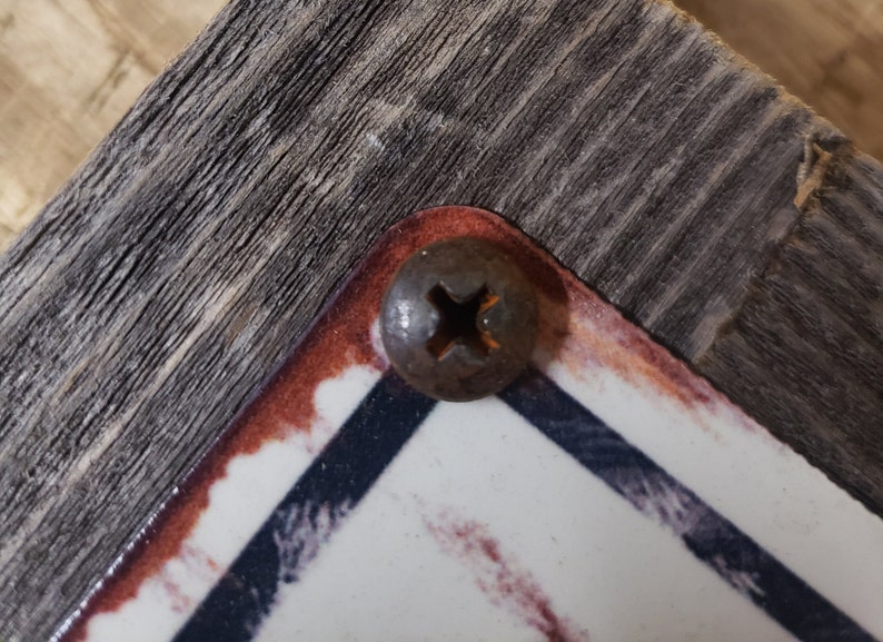 Puede incluir: Primer plano de un tornillo oxidado con cabeza de cruz, que sujeta una pieza de madera a una superficie con un patr&oacute;n blanco y azul.