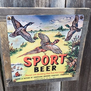 May include: A vintage wooden sign with a colourful illustration of three birds and a pheasant. The sign advertises "Sport Beer" brewed with Sparkling Deep Rock Wall Water. The text reads "Brewed & Bottled by Sebewaing Brewing Company, Sebewaing, Mich. Contents 12 fl. oz."