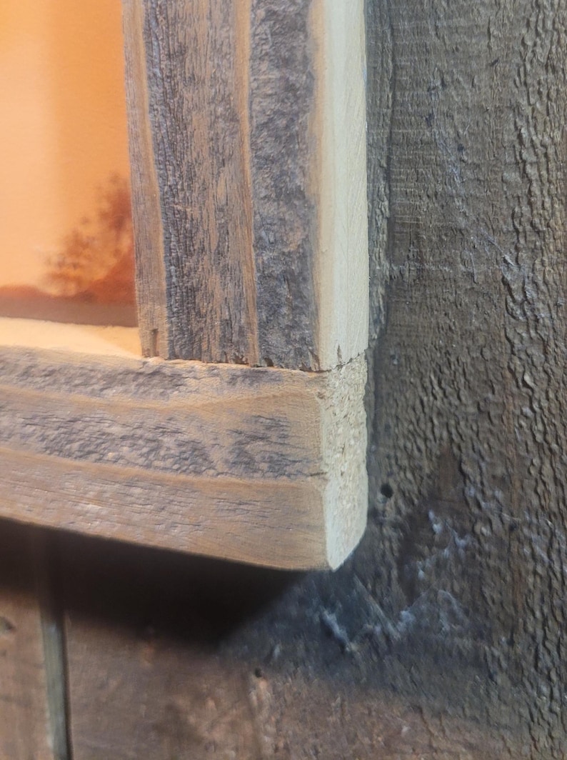 May include: Close-up of a corner of a rustic wooden picture frame. The frame is made of reclaimed wood with a natural gray finish. The wood has a rough texture and shows signs of wear and tear.