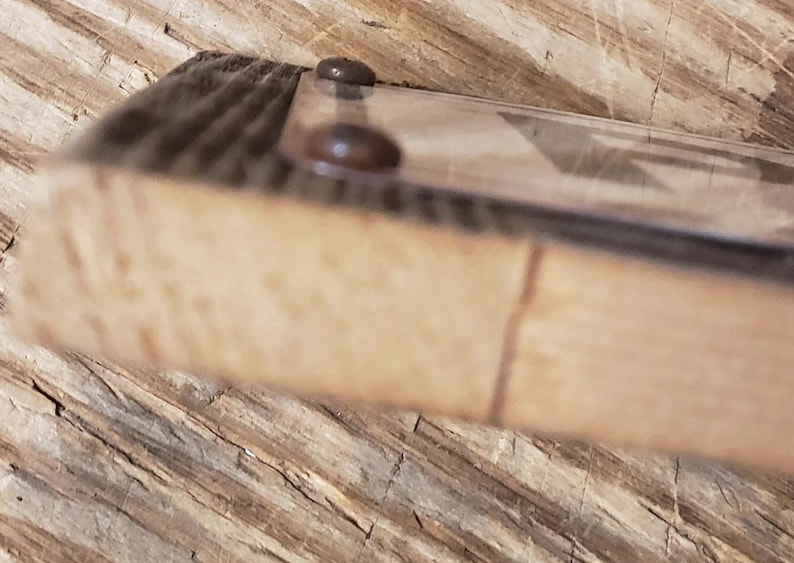 May include: Close-up of a wooden frame with a clear glass or plastic cover. Two small, dark-colored fasteners secure the cover to the frame. The wood has a natural, light brown color with visible grain.