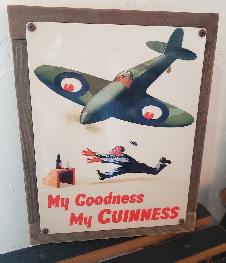May include: A vintage metal sign with a green and white image of a plane flying over a man running towards a glass of beer. The sign reads "My Goodness My Guinness".