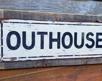 Peut inclure: Une pancarte en bois rustique avec une plaque en métal blanc sur laquelle est inscrit "OUTHOUSE" en lettres noires. La pancarte a un aspect vieilli avec des grains de bois et des têtes de clous visibles.