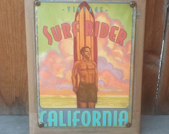 May include: Vintage Surf Rider California sign with a surfer standing on a surfboard in front of a sunset sky. The sign is made of metal and has a wood frame.