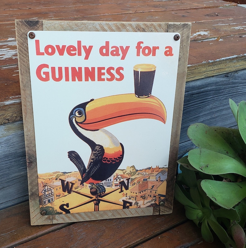 Puede incluir: Un letrero de madera con un anuncio vintage de Guinness que muestra un tuc&aacute;n sosteniendo un vaso de Guinness. El letrero dice "Lovely day for a GUINNESS".
