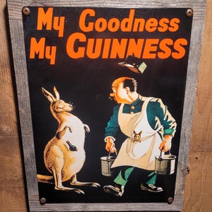 May include: Vintage Guinness advertisement sign featuring a kangaroo and a man in an apron. The sign reads "My Goodness My GUINNESS" in orange lettering. The man is carrying buckets, and the kangaroo has a bottle in its pouch. The sign is framed in a wooden border.