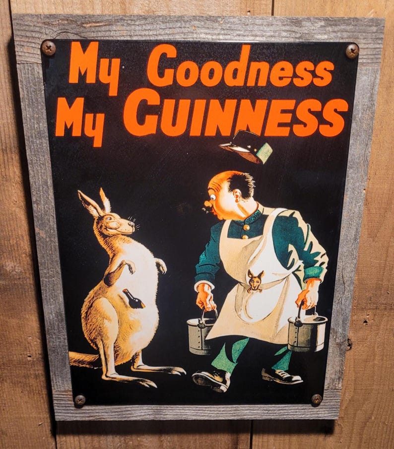 May include: Vintage Guinness advertisement sign featuring a kangaroo and a man in an apron. The sign reads "My Goodness My GUINNESS" in orange lettering. The man is carrying buckets, and the kangaroo has a bottle in its pouch. The sign is framed in a wooden border.