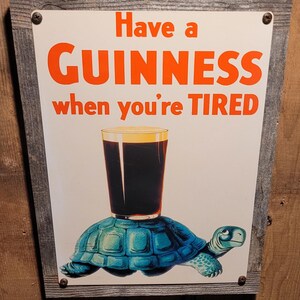May include: A framed sign with the text "Have a GUINNESS when you're TIRED" in orange letters. The image features a pint of Guinness balanced on a blue turtle. The frame is made of weathered wood.