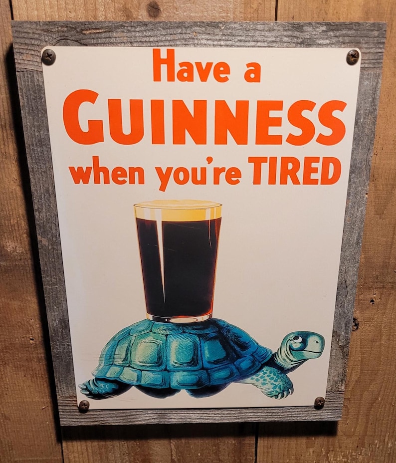 May include: A framed sign with the text "Have a GUINNESS when you're TIRED" in orange letters. The image features a pint of Guinness balanced on a blue turtle. The frame is made of weathered wood.