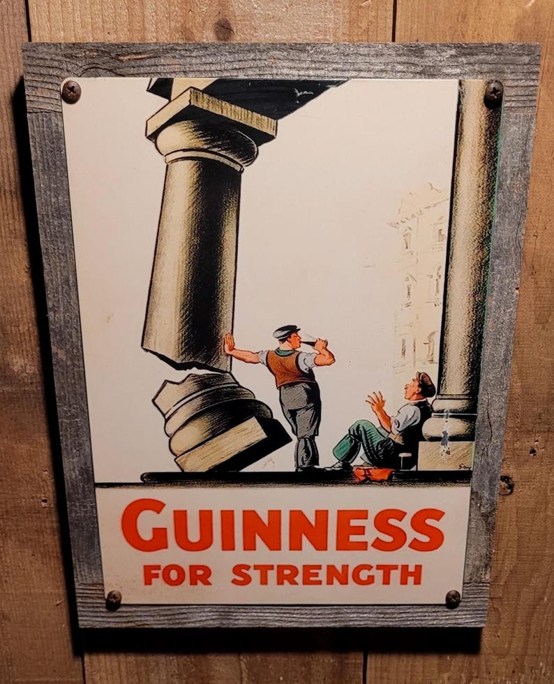 May include: Vintage Guinness advert sign in a wooden frame. The sign shows an illustration of two men and a broken column, with the words "GUINNESS FOR STRENGTH" in red.