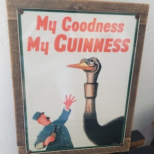 Puede incluir: Un letrero de metal vintage con un marco de madera marr&oacute;n. El letrero presenta una ilustraci&oacute;n de dibujos animados de una avestruz con un cuello largo y un hombre sosteniendo una botella de Guinness. El texto en el letrero dice "My Goodness My GUINNESS".