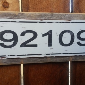 May include: A rustic wooden sign with a white metal plaque featuring the number 92109 in black.