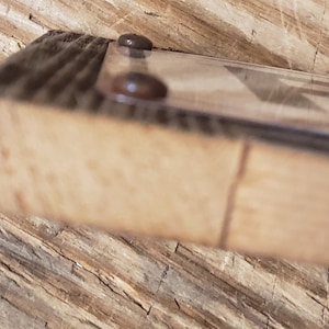 Puede incluir: Primer plano del borde inferior de un marco de imagen de madera con dos sujetadores met&aacute;licos de color marr&oacute;n oscuro. El marco est&aacute; hecho de madera recuperada con veta de madera natural.