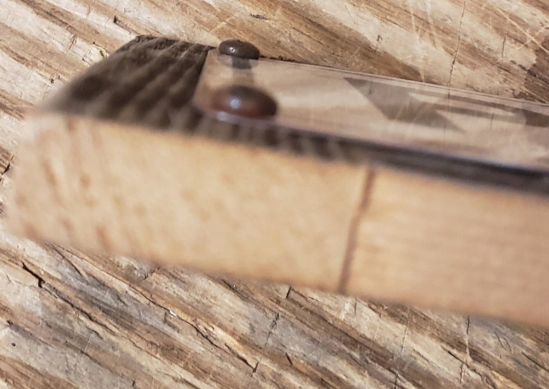 Puede incluir: Primer plano del borde inferior de un marco de imagen de madera con dos sujetadores met&aacute;licos de color marr&oacute;n oscuro. El marco est&aacute; hecho de madera recuperada con veta de madera natural.