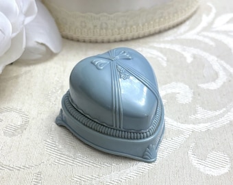 May include: A light blue heart-shaped ring box with a decorative bow on the lid. The box is made of plastic and has a satin-like finish.