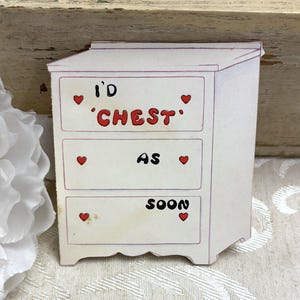 May include: A white rectangular sticker shaped like a three-drawer chest with red outlines and small red hearts on each drawer. The text on the drawers reads I'D 'CHEST' AS SOON in black and red lettering. The sticker has a flat, matte finish.