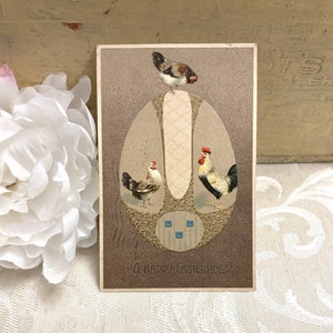 May include: Vintage Easter postcard featuring three chickens, two hens and a rooster, standing on a large egg with a gold and blue design. The text "A Happy Eastertide" is printed at the bottom of the postcard.