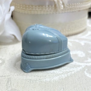 May include: A light blue plastic ring box with a heart-shaped lid. The box has a decorative trim around the edge and a small design on the front.