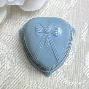 May include: A light blue heart-shaped ring box with a raised bow design and a beaded trim.