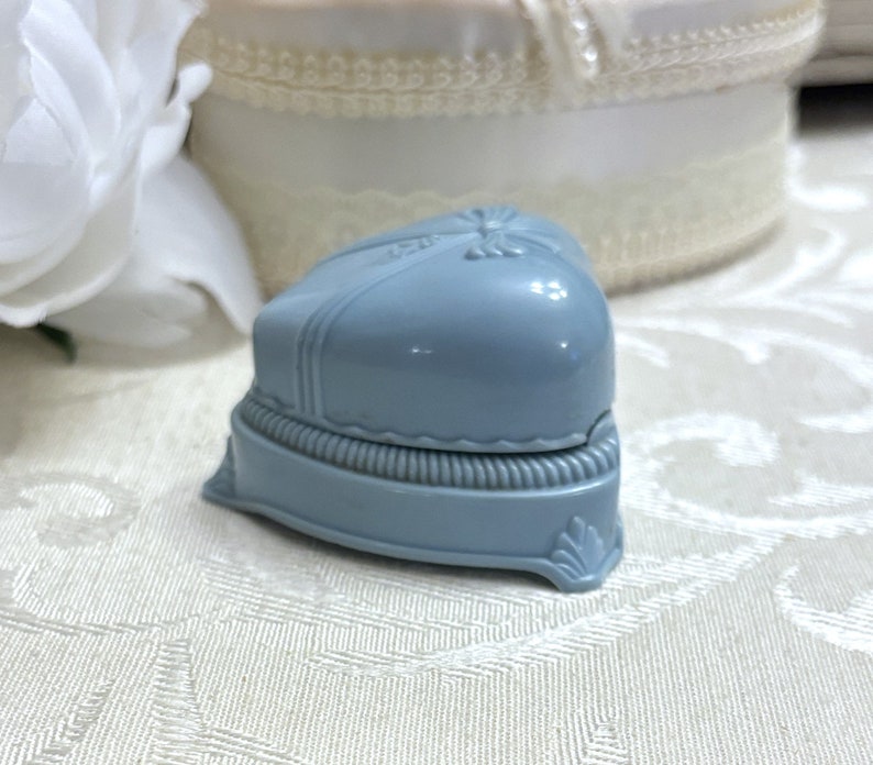May include: A light blue heart-shaped ring box with a raised design and a scalloped edge.