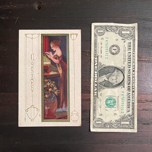 K&ouml;nnte beinhalten: Eine Vintage-Postkarte mit einer Frau in einem langen Kleid, die ein Buch liest. Die Postkarte hat einen goldenen Rand und das Wort "Constancy" steht vertikal auf der linken Seite.
