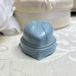 May include: A light blue ring box with a heart-shaped lid and decorative details. The box is made of plastic and has a vintage look.