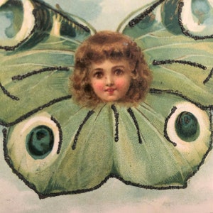 Puede incluir: Ilustraci&oacute;n vintage de la cara de un ni&ntilde;o rodeada de alas de mariposa. Las alas son principalmente verdes con detalles de purpurina negra. El ni&ntilde;o tiene cabello casta&ntilde;o rizado y mejillas rosadas, sobre un fondo azul claro.