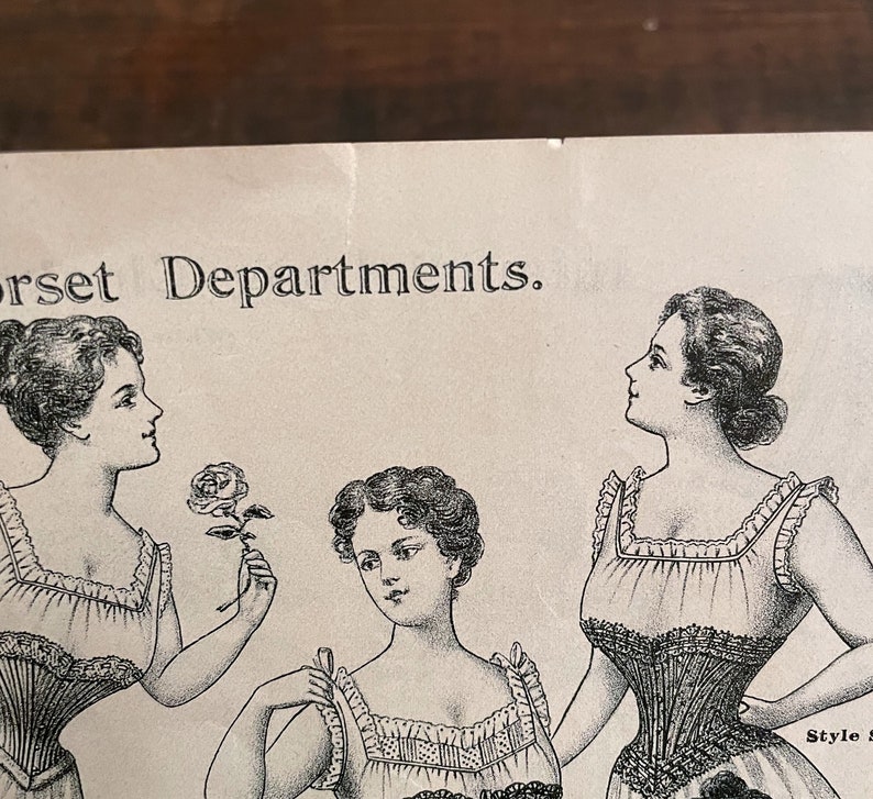 May include: Black and white illustration of three women wearing corsets. The text "Corset Departments" is at the top of the image.