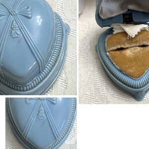 May include: A light blue heart-shaped ring box with a velvet interior. The box has a decorative bow and floral design on the lid.