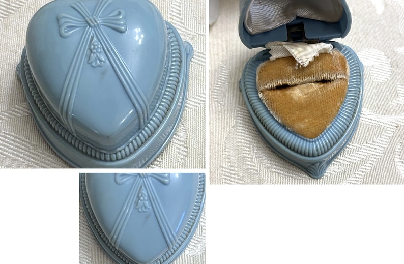 May include: A light blue heart-shaped ring box with a velvet interior. The box has a decorative bow and floral design on the lid.