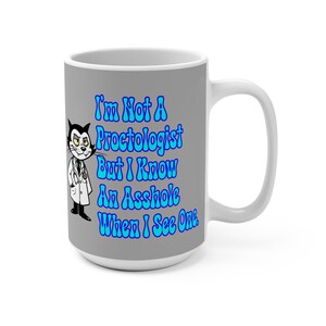 May include: A white ceramic mug with a grey background and a humorous message in blue text: "I'm Not A Proctologist But I Know An Asshole When I See One." A cartoon cat in a doctor's coat and stethoscope is on the left.