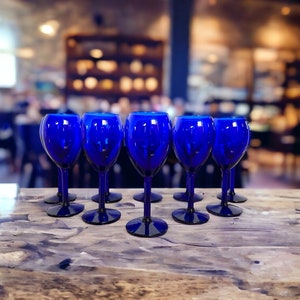May include: A row of eight cobalt blue wine glasses sit on a wooden table. The glasses are arranged in a staggered pattern, with the tallest glass in the center.