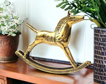 May include: A gold-colored rocking horse figurine with intricate details. The horse is standing on a wooden base with a rocking motion.