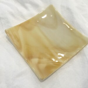 May include: A square, decorative dish with a diamond shape. The dish is made of a translucent material with a marbled pattern of light beige and cream colors. The dish has a glossy finish.