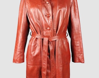 Può includere: Un cappotto vintage in pelle color ruggine con chiusura a bottoni e cintura abbinata. Il cappotto presenta un colletto classico, maniche lunghe e tasche. Il cappotto è esposto su un manichino.