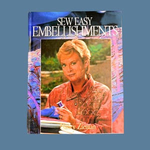 May include: A book titled "Sew Easy Embellishments" with a woman in a pink shirt holding a spool of thread. The book cover features a colorful background with a floral design.