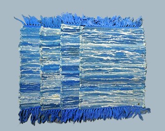 May include: A blue and white woven rug with fringe on all sides. The rug is made of recycled materials and has a rustic, handmade look.