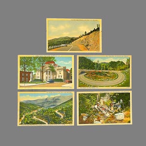 May include: Five vintage postcards depicting scenic views of the Blue Ridge Mountains in North Carolina. The postcards feature images of a courthouse, a winding road, a mountain pass, a scenic overlook, and a group of people cooking outdoors.