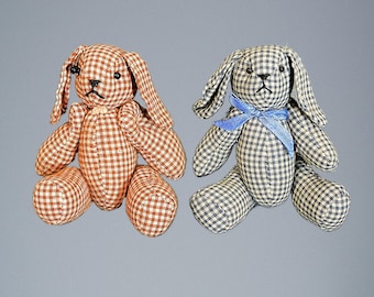 May include: Two gingham fabric bunny plushes. One is brown and white gingham with black eyes and a black nose. The other is blue and white gingham with black eyes and a black nose. The blue bunny has a blue ribbon around its neck.