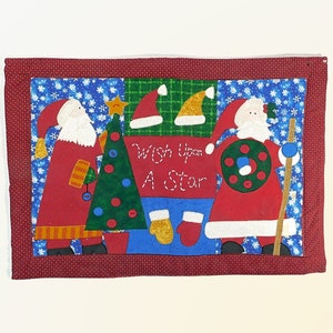 May include: A red and green Christmas-themed quilted wall hanging with two Santa figures, a Christmas tree, and the text "Wish Upon A Star".