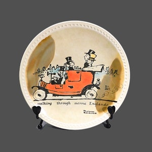 May include: Decorative plate featuring a vintage car with passengers, in orange and black. The plate has a cream-colored background with the text "walking through merric Englande". The plate has a beaded rim.