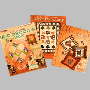 May include: Three quilting pattern books with colorful covers. The first book is titled "Ginny Fraser's Quilt Collection for Baby" and features a baby quilt with a variety of animal designs. The second book is titled "Holiday Homecoming" and features a quilt with a holiday theme. The third book is titled "Pillow Patches and other possibilities" and features a variety of pillows with different designs.