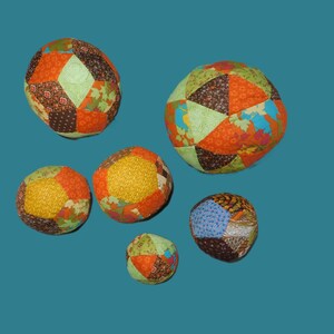 May include: Six colourful patchwork fabric balls of various sizes. The balls are made of different fabrics in shades of orange, brown, green, yellow, and blue.