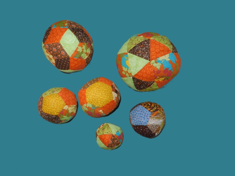 May include: Six colourful patchwork fabric balls of various sizes. The balls are made of different fabrics in shades of orange, brown, green, yellow, and blue.